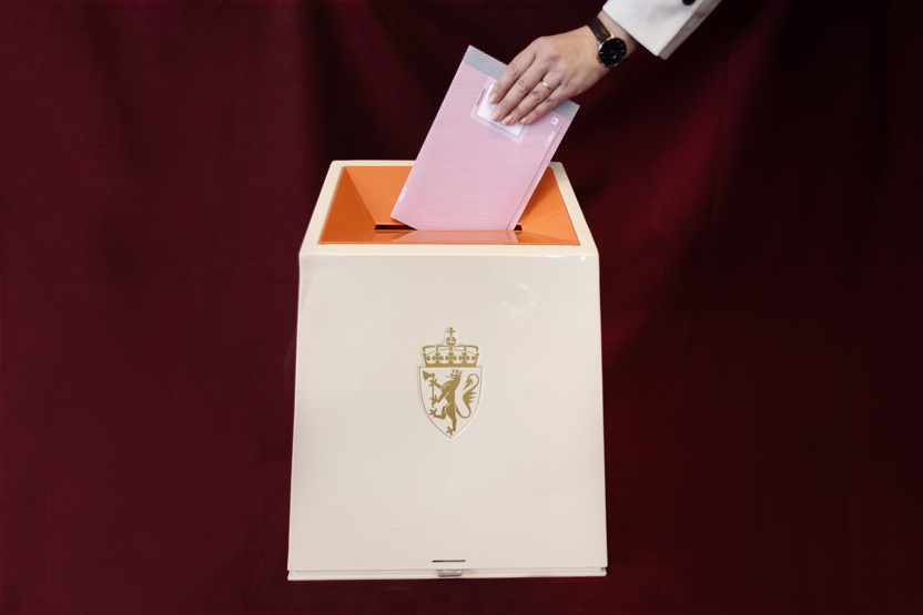 En valgurne mot rød bakgrunn. En hånd putter en stemmeseddel oppi.