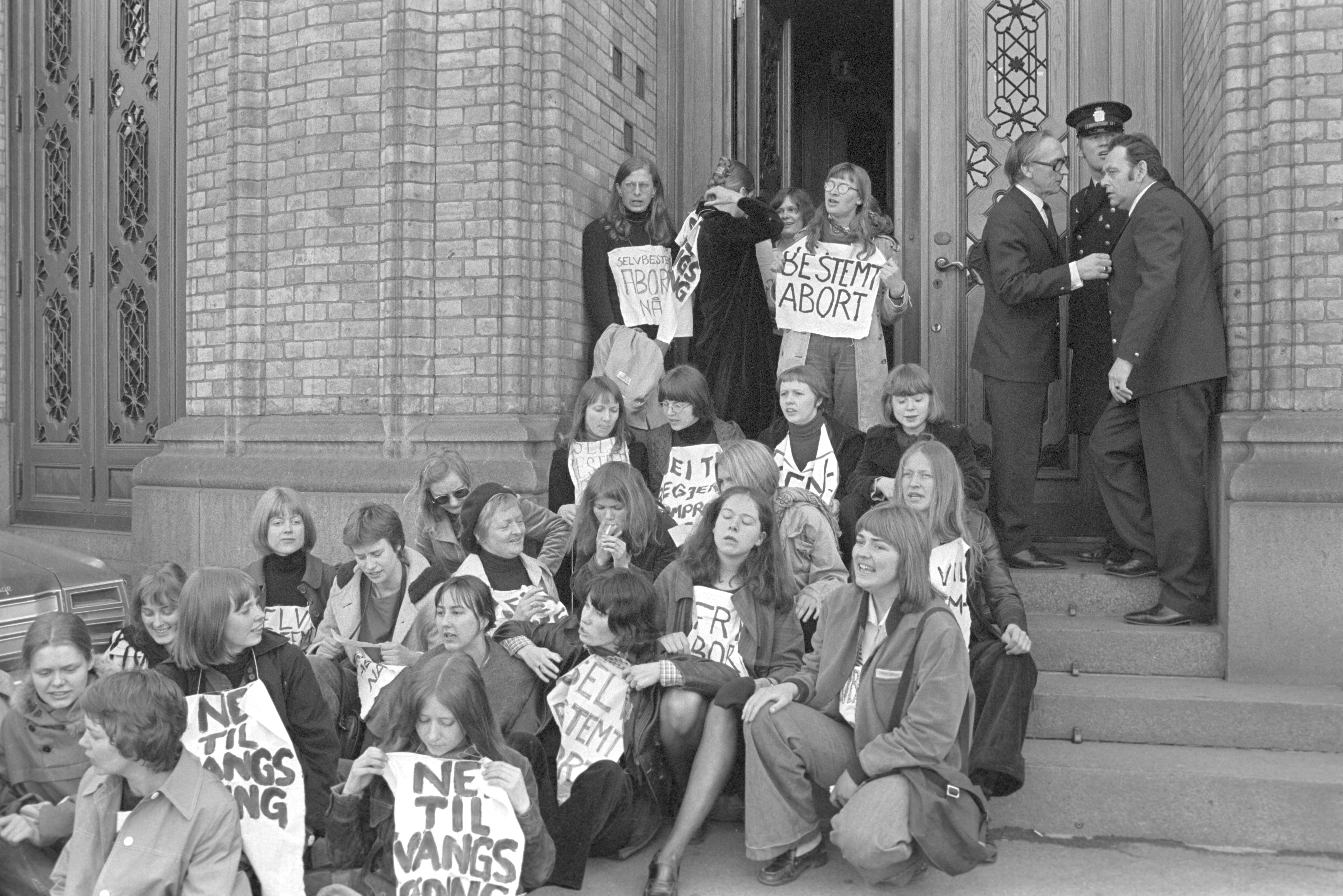 Kvinner sitter på trapp utenfor Stortinget og demonstrerer for selvbestemt abort. Foto i svart hvitt.