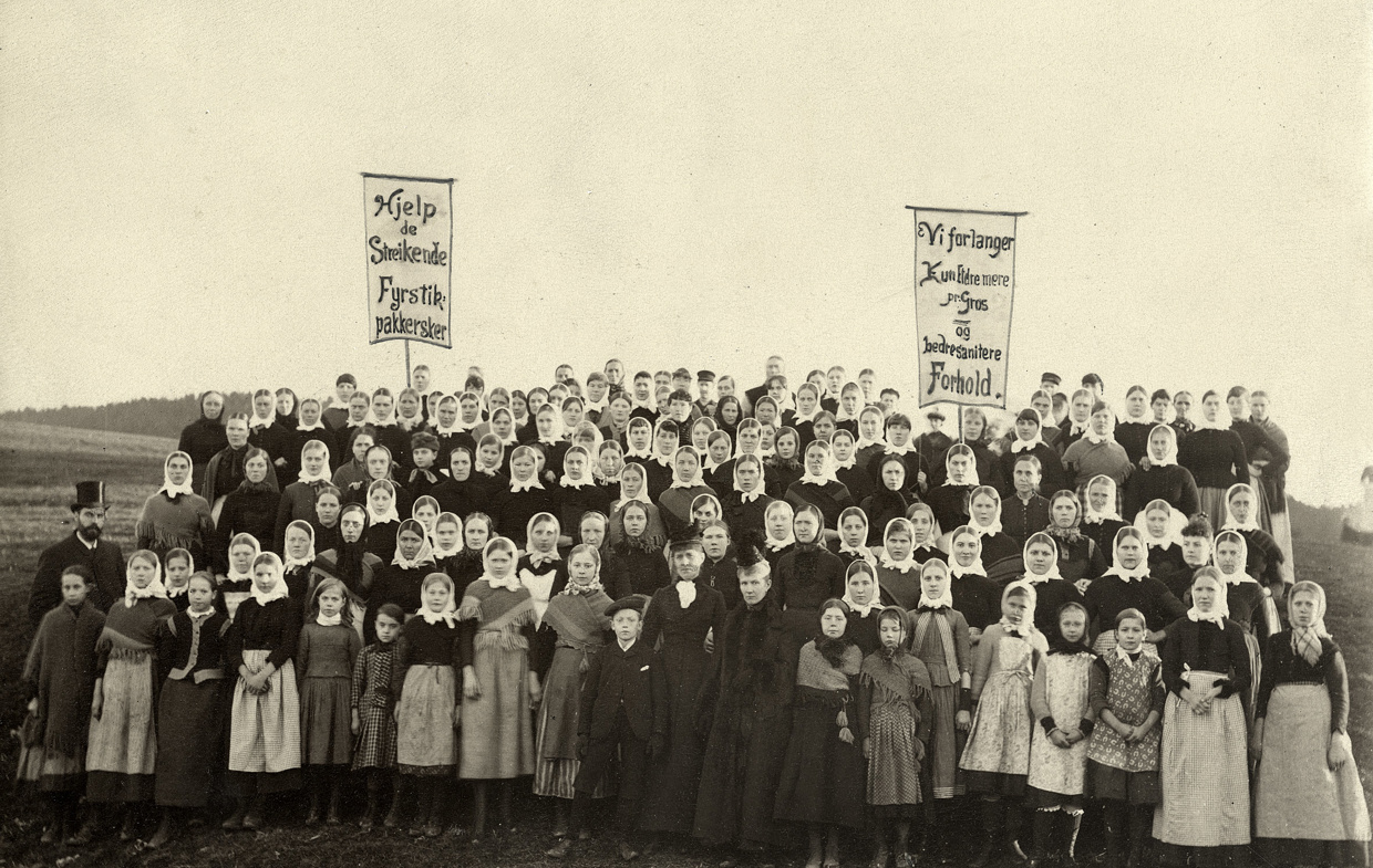 En stor gruppe med kvinnelige fyrstikkarbeidere demonstrerer for sine rettigheter. De bærer faner med påskriften "Hjelp de streikende fyrstikkpakkersker" og "Vi forlanger bedre sanitære forhold".