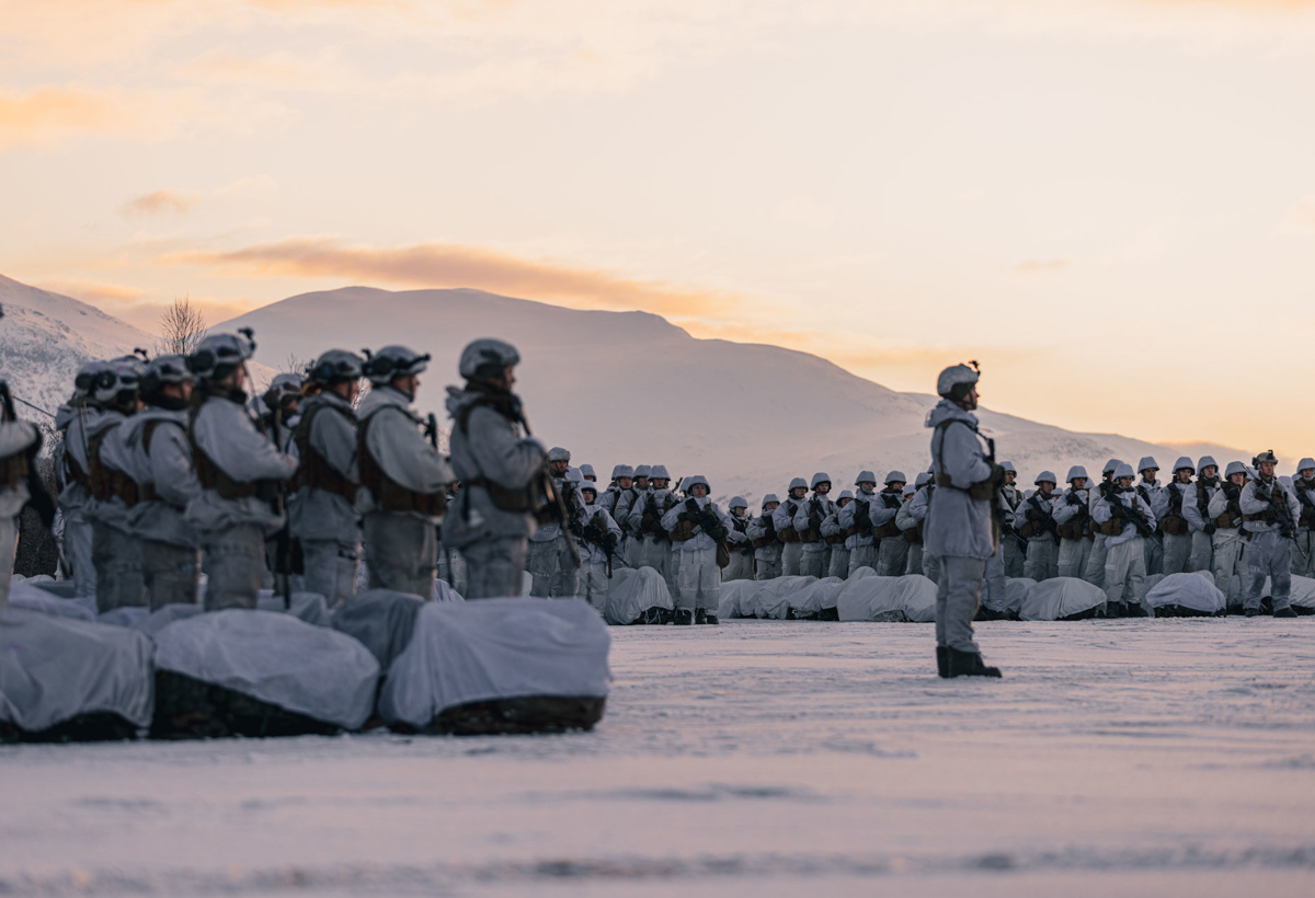 Soldater står i snøen med fjell i bakgrunnen.