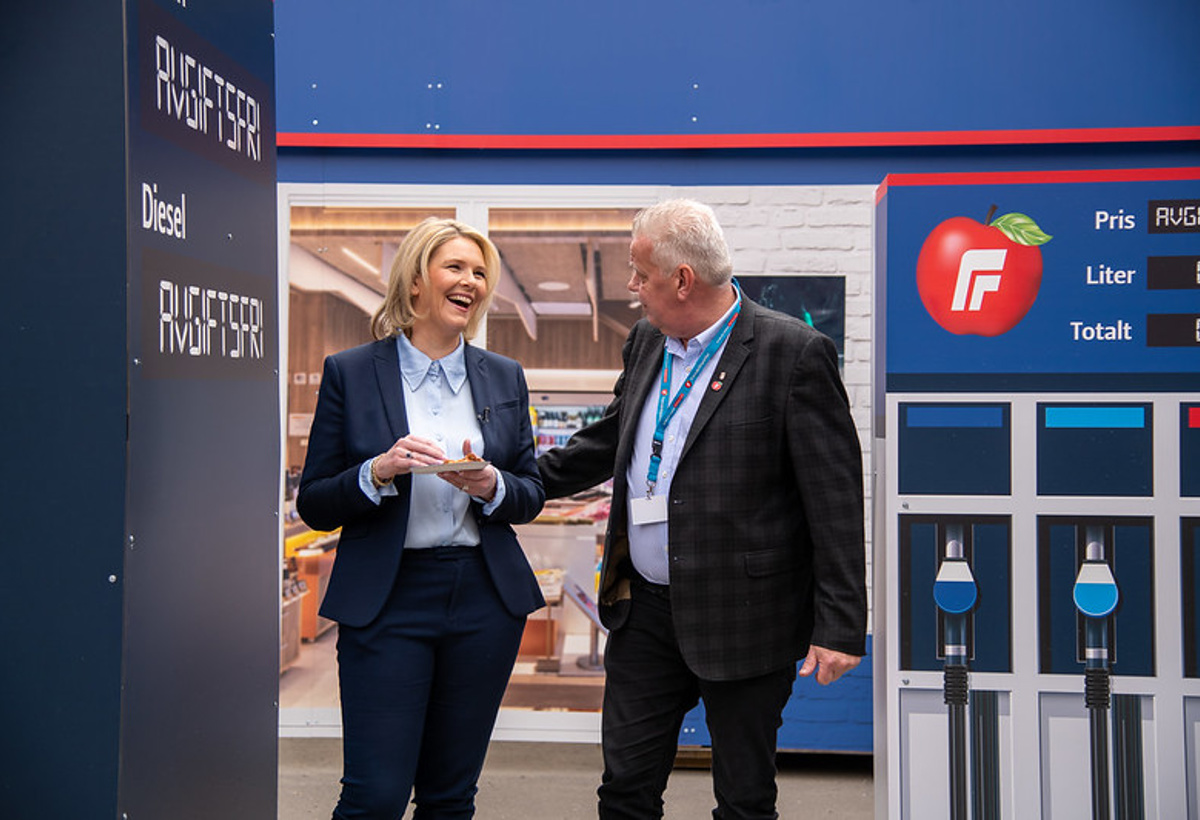 En mann og en kvinne smiler til hverandre ved bensinpumper med logoen til Fremskrittspartiet,