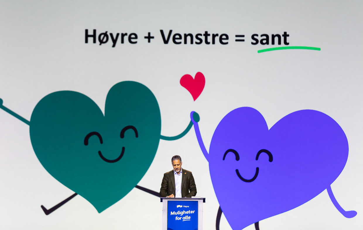 En mann står på en talerstol. På skjermen bak står det Høyre + Venstre = sant.