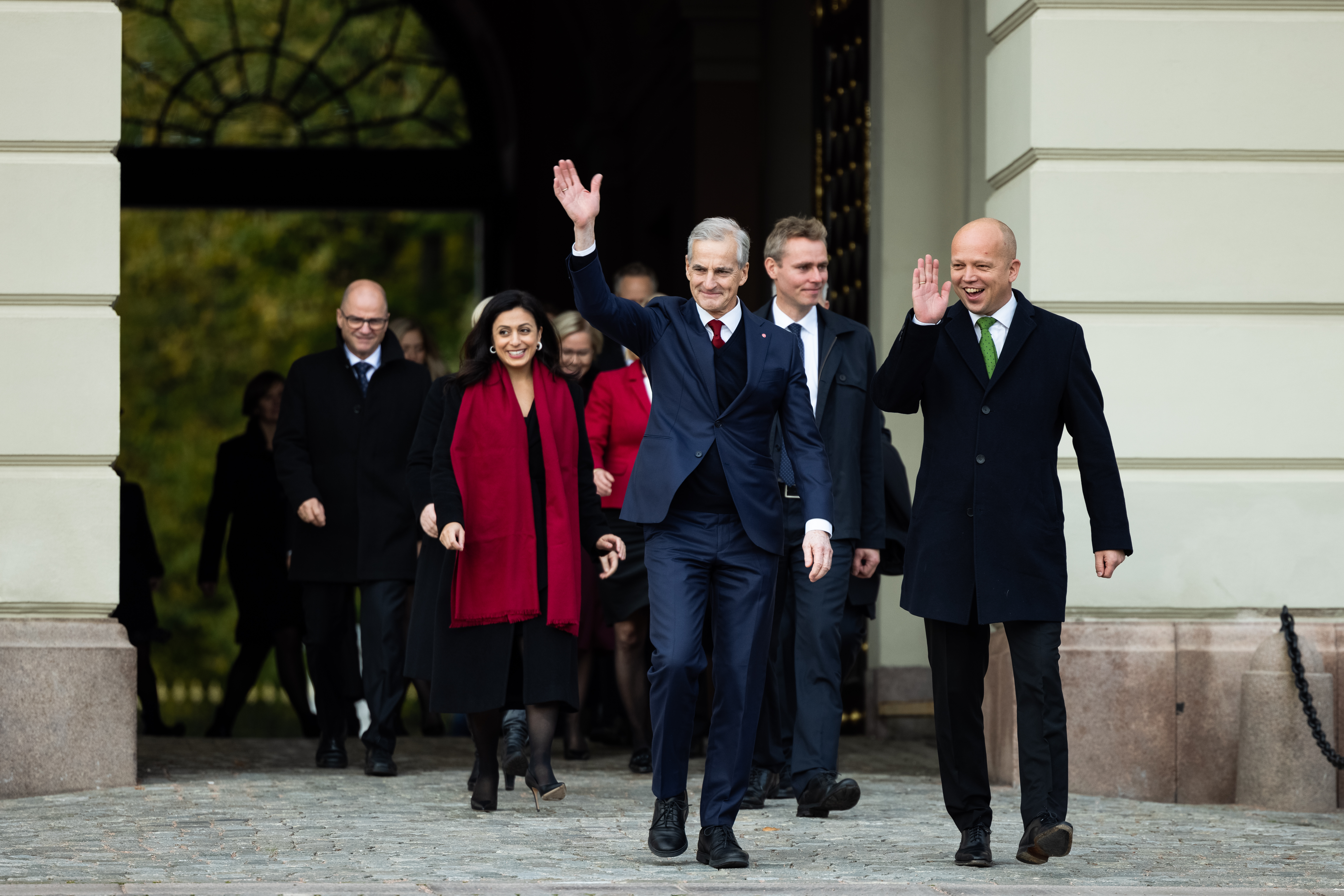 En gruppe mennesker kommer smilende og vinkende ut på slottsplassen.