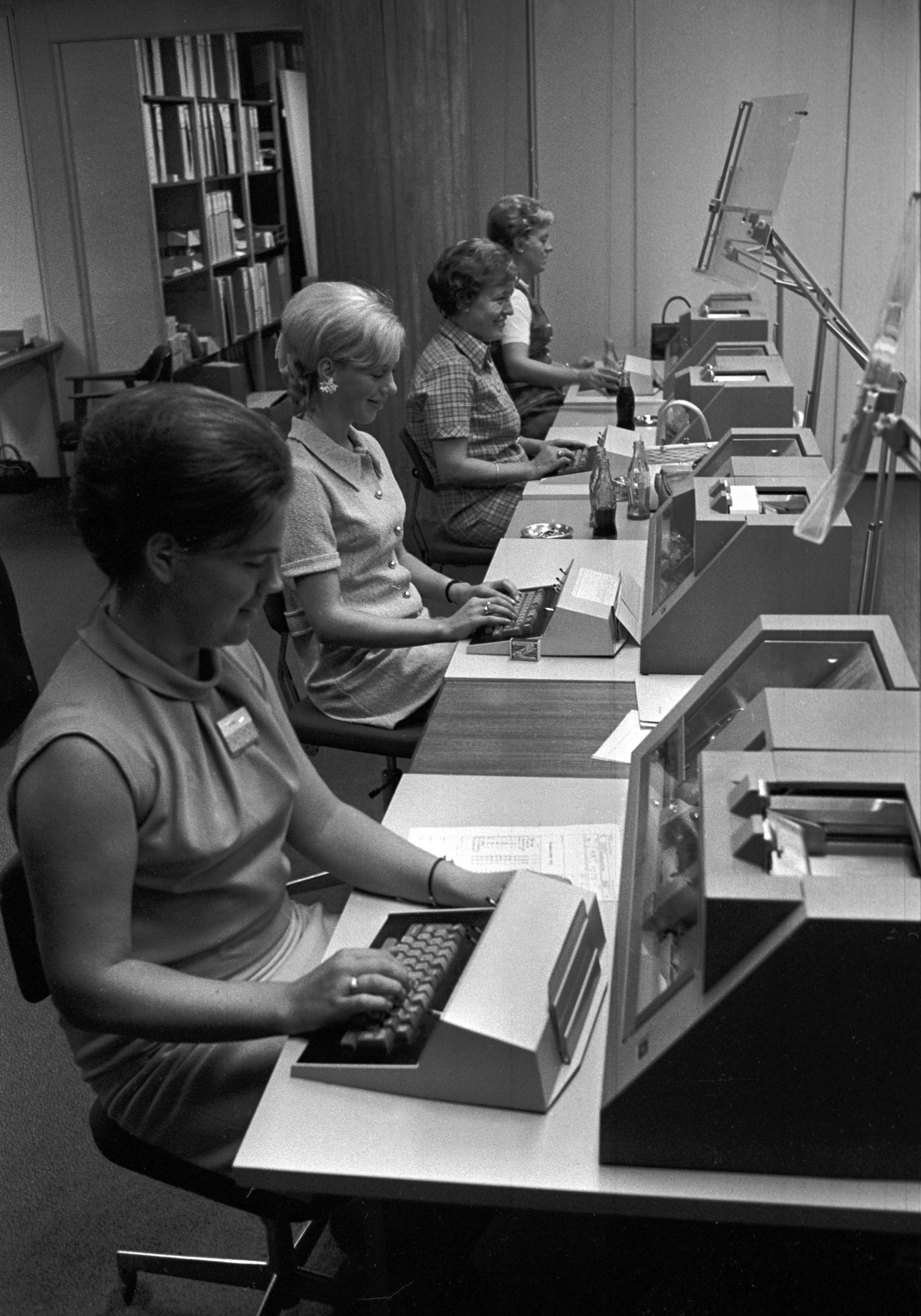 Svart hvitt bilde. Fire damer sitter foran regnemaskiner.