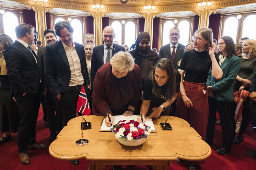 Mange stortingsrepresentanter står rundt et bord og venter på å signere. 